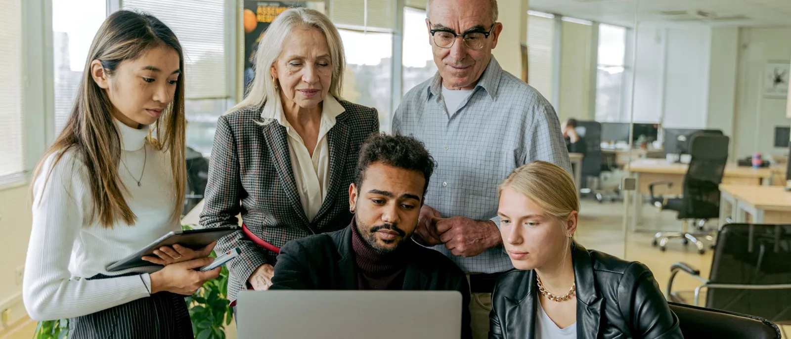 A multigenerational team gathered around a laptop in a bright office